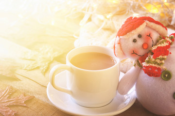 White cup with hot chocolate, snowman and christmas lights