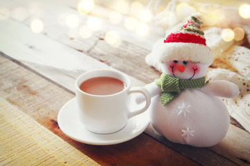 White cup with hot chocolate, snowman and christmas lights