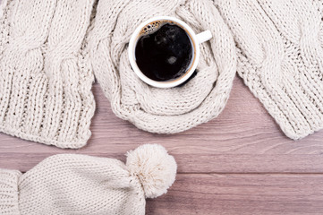 Handmade knitted wool scarf and cap. Winter clothes. Hot coffee cup on wooden background. Concept cozy atmosphere with a cup of coffee in winter