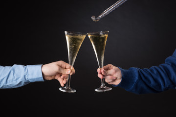 Two male hands holding champagne glasses and foil blowout isolated on black background