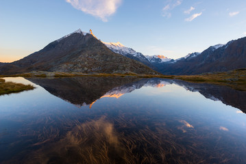 High altitude alpine lake in idyllic land with reflection of majestic rocky mountain peaks glowing at sunset. Wide angle view on the Alps.