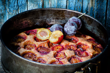 Plum tart in baking dish, fresh plums on top