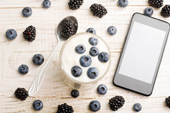 Yogurt with blueberries, a smartphone, a teaspoon of blackberry