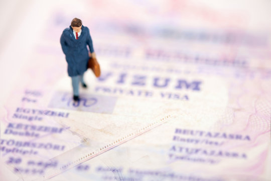 Toy businessman / View of miniature toy, businessman walking on passport. Travel concept.