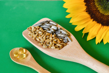 Sunflower seeds and vitamin E supplement on wood spoons, arranged diagonally and viewed from above,...
