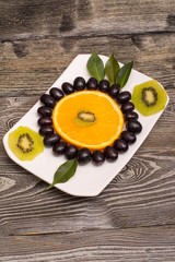 slice of orange, black grapes, kiwi on a white plate, wooden background