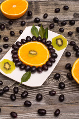 slice of orange, black grapes, kiwi on a white plate, wooden background