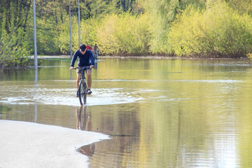 cyclist try to ride a bike during a flood at springtime. asphalt road under water as river overflow