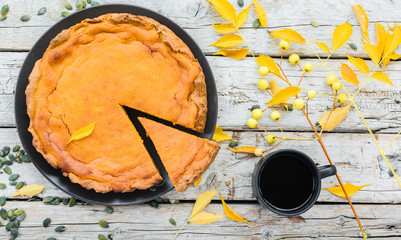 Pumpkin pie for Thanksgiving day and cup of black coffee on autumn leaves and wooden background