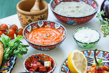 Fototapeta na wymiar Small bowls of homemade harissa and tzatziki with meze on a table