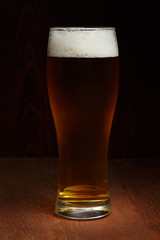 Dark beer in glass standing at wooden background