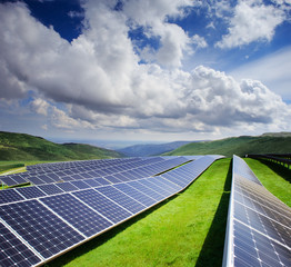 Solar station in green field under blue cloudy sky with mountain
