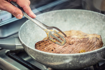 Beef steak. Chef in a restaurant kitchen use ceramic pan for preparation of beef steak.