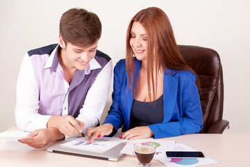 Two young happy smiling successful businesspeople working with document or contract at office