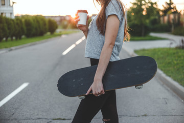 beautiful girl drinks from white to-go cup holding skateboard