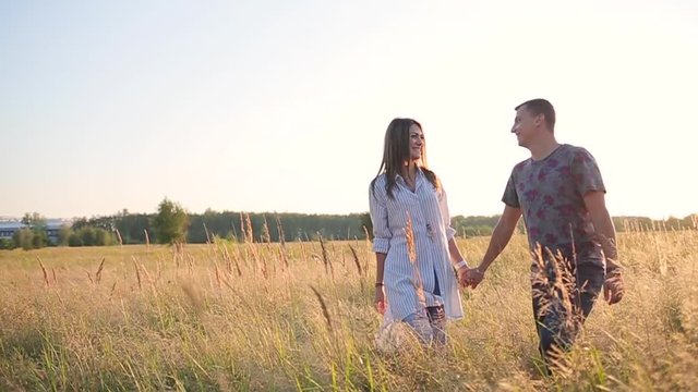 couple walking holding hands in the grass field.