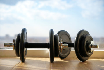 Obraz na płótnie Canvas Dumbbells on the background of windows and the big city and sky.