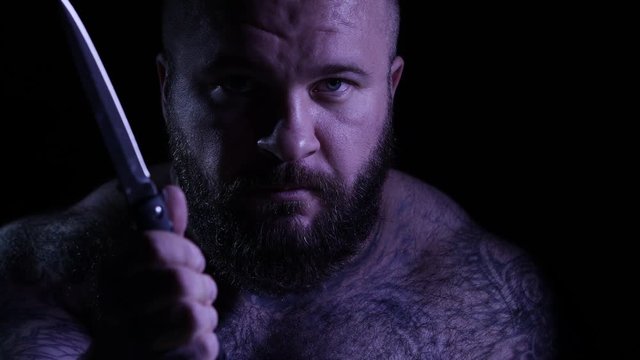 Bald tattoed bearded muscular gangster with a knife. 4K UHD