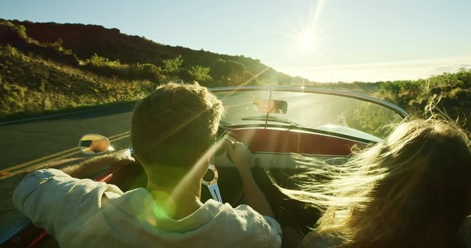 Happy couple driving on country road into the sunset in classic vintage sports car