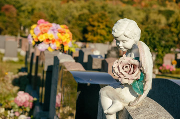 Statue of an angel holding a rose sitting on a tombstone in a cemetery