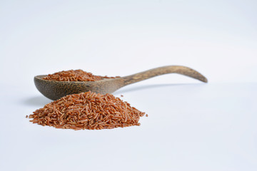 Uncooked red rice in a wooden spoon, white background