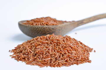 Uncooked red rice in a wooden spoon, white background 