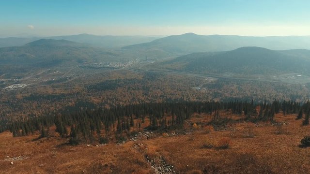 Aerial View from the mountain peak. Mountains in the fall. Burnt grass. Trees in mountain. The village at the foot of the mountain. The range of accommodation Shor (indigenous people of Siberia)