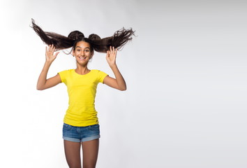Emotional young brunette girl with long hair in yellow shirt on a white background