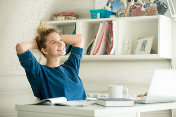 Portrait of an attractive woman at the table with cup and laptop, book, notebook on it, arms...