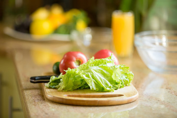 Wooden cutting board on the table with fresh vegetables on, orange juice on the background