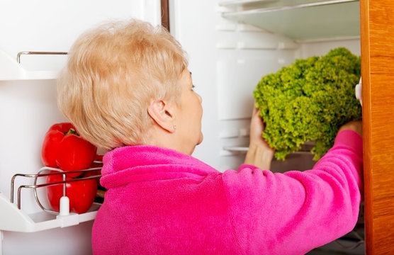 Senior woman taking a green lettuce from fridge