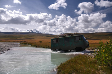 Off-road car moving mountain river at a ford on the background of snowy peaks, Plateau Ukok, Altai...