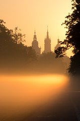 Fototapeta premium Misty Blonia meadow in Krakow, Poland, with St Mary's church and Town Hall towers in the background.
