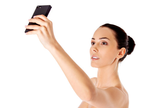 Nude beautiful woman taking selfie on white background.