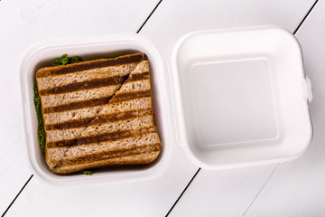 Hot sandwich in a plastic bowl on white wooden background