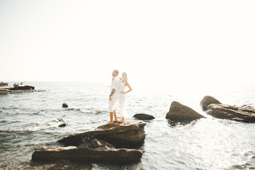 Wedding couple kissing and hugging on rocks near blue sea