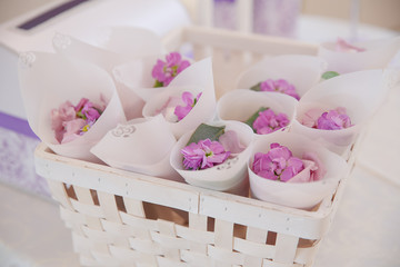 Violet petals lie in white envelopes in a basket