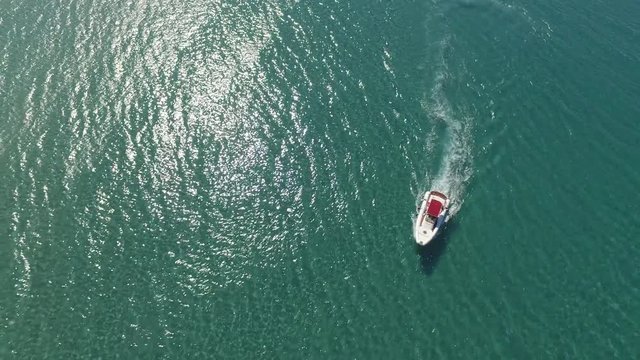 Vessel approaching a dinky nearby a big rock. Few girls suntanning a on bard. Sun reflection with small waves on water surface.