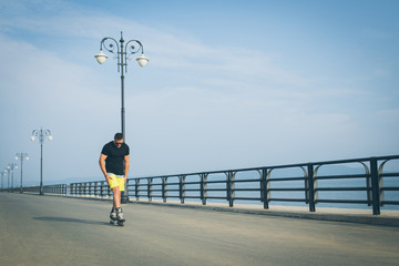 young man with inline skates ride in summer park seafront outdoor rollerskater