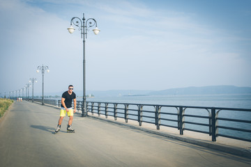 young man with inline skates ride in summer park seafront outdoor rollerskater
