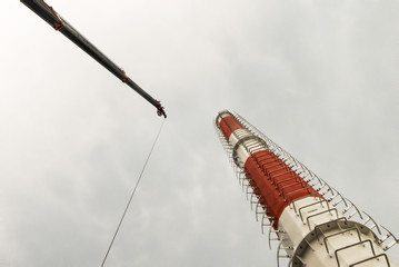 View of progress of erecting red and white bands telecommunication tower or monopole with crane boom and hoisting cable
