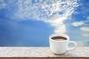 white cup of coffee on wooden over blue sky and cloudy on day noon light background.
