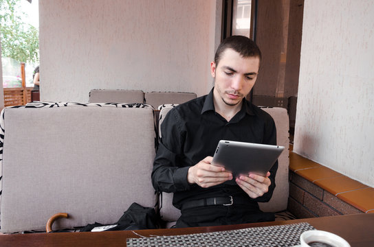 Happy businessman in black suit with digital tablet at the cup of coffee in cafe