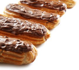 Delicious chocolate eclairs in row on white background, closeup