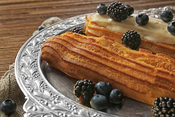 Delicious eclairs with berries in silver tray on bagging and wooden background