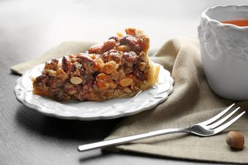 Tasty piece of nut cake on plate and cup of tea on table