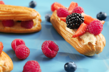 Delicious eclairs and berries on blue background