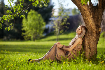 Beautiful young woman dressed in boho style sitting on green gra