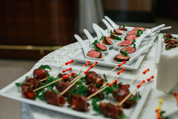 Spoons with baked meet and meet on sticks lie on the square whit