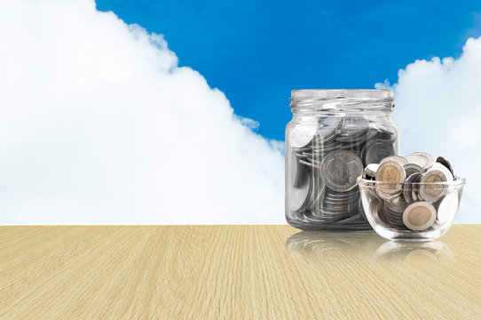 coins in a glass jar on Wood floor ,savings coins - Investment And Interest Concept saving money concept, growing money on piggy bank. isolated on blue sky background